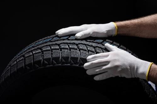 A winter tire being rolled by a technician wearing white gloves.